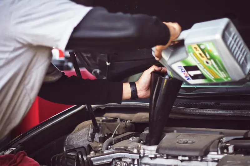 Mechanic topping up engine oil during a car service in Billingshurst